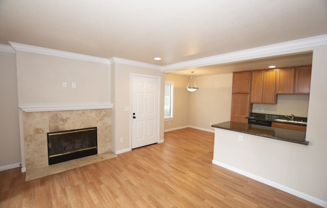 View from living area into kitchen and dining area with wood look flooring, fireplace, stone counters, brown cabinets, black appliances, and recessed lighting