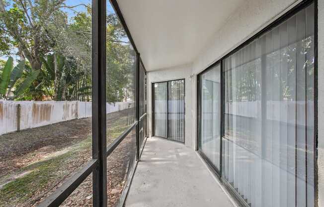 A long, narrow balcony with glass railings and a view of trees and a fence.