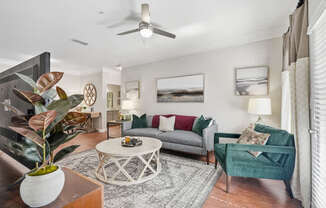A living room with a grey couch, a green armchair, a coffee table, and a plant in a white vase.