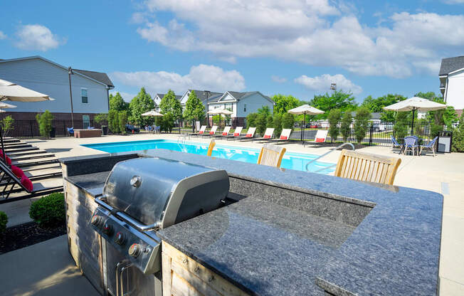 A BBQ grill is in the foreground of a pool area.