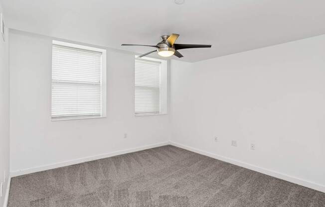 A room with a ceiling fan and two windows.