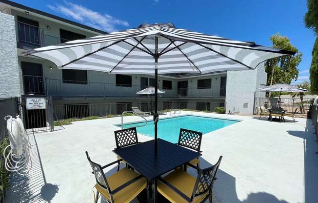 a patio with a table and chairs and a pool in the background