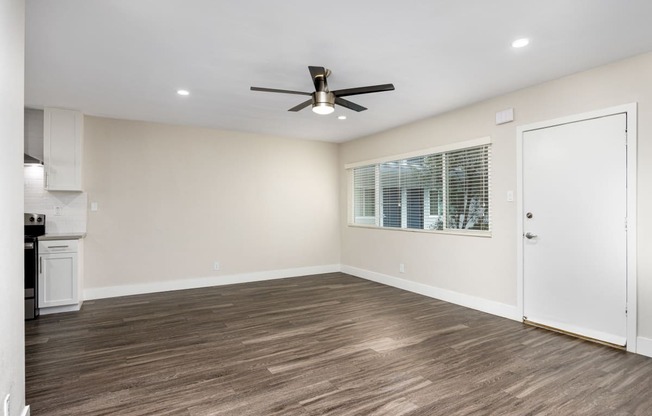 an empty living room with a ceiling fan and a kitchen
