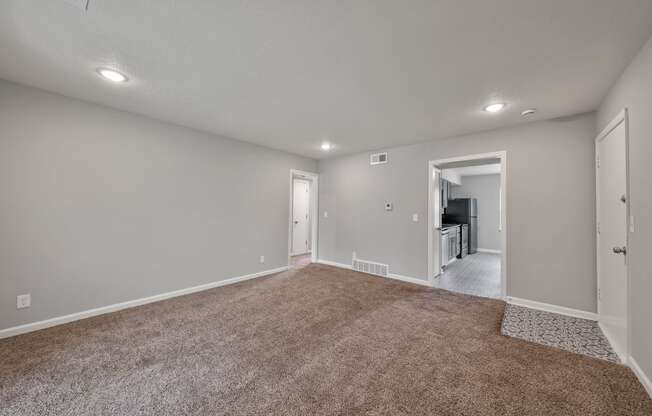 an empty living room with carpet and a door to a kitchen