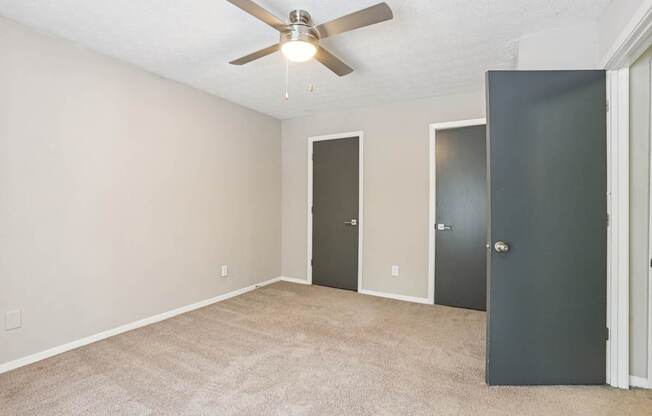 A room with a ceiling fan and three doors.