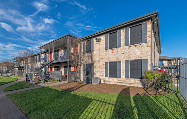 An exterior photo of a two-story apartment  building (Costa Mesa Apartments) with stairs and greenery space