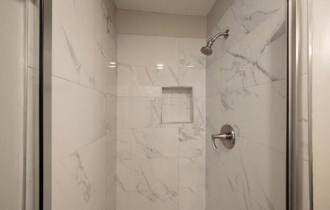A white marble bathroom with a shower and a door.