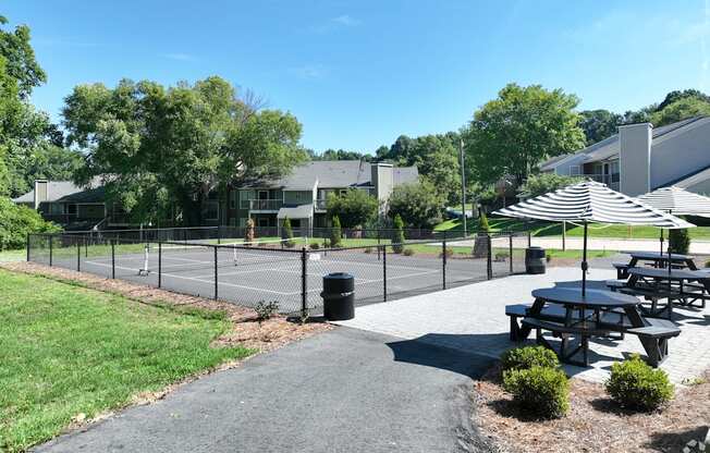 A sunny day at a park with picnic tables and a tennis court.