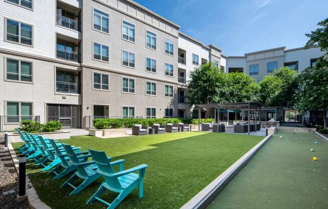 a courtyard with green grass and blue chairs in front of a building