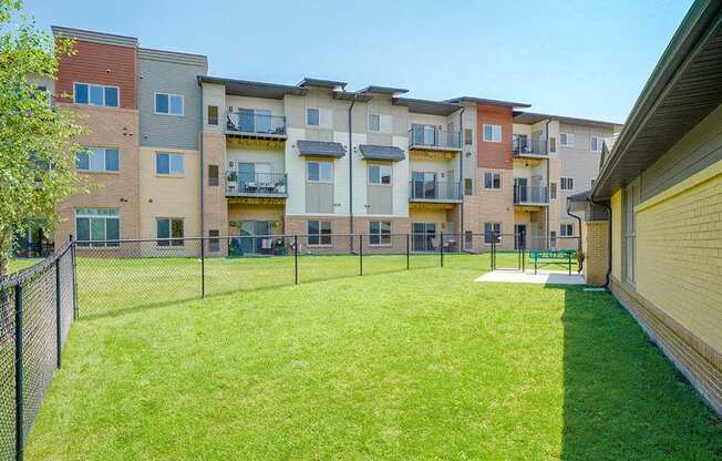 A fenced-in grassy dog park with a bench and plenty of room for your dog to run around off leash.