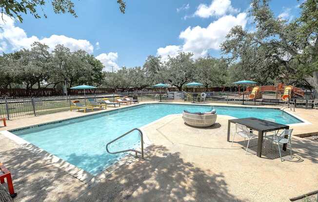 A large outdoor swimming pool surrounded by trees and a fence.
