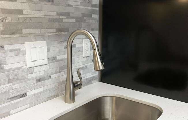 a kitchen sink with a stainless steel faucet in front of a tile wall