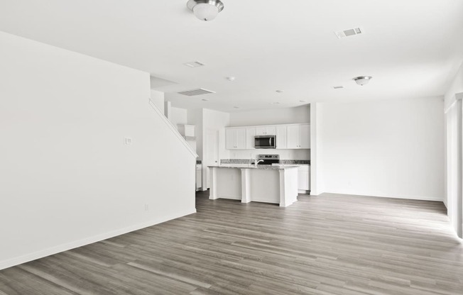 a spacious family living room and kitchen with white walls and wood floors