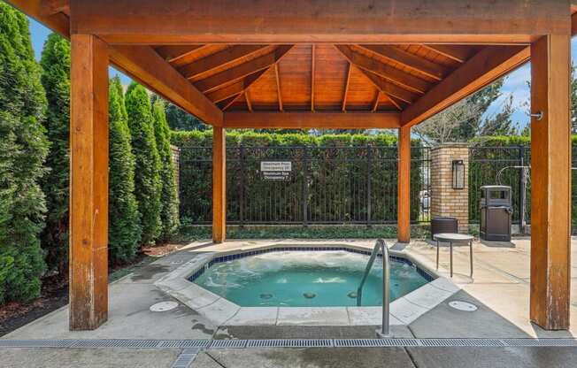 a hot tub is under a wooden pavilion next to a pool