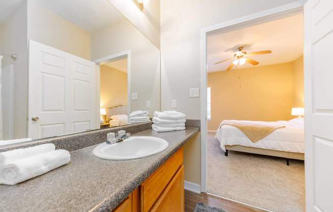 A bathroom with a sink, mirror, and a bedroom in the background.