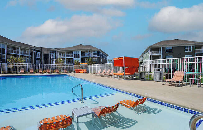 A swimming pool with orange chairs and a red object in the background.