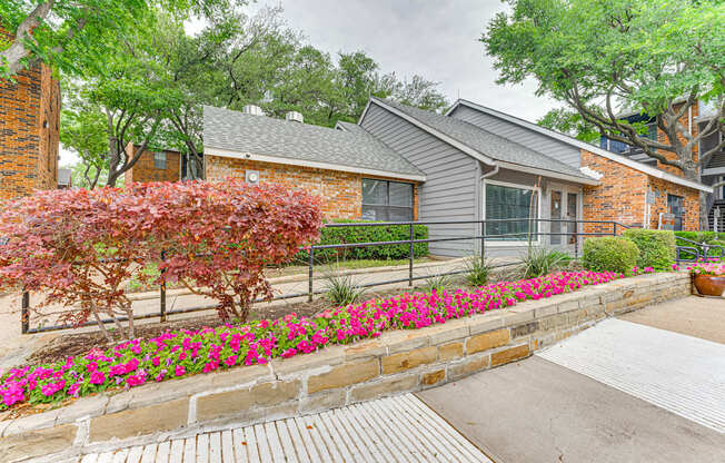 A house with a grey roof and a brick wall with a flower bed in front.