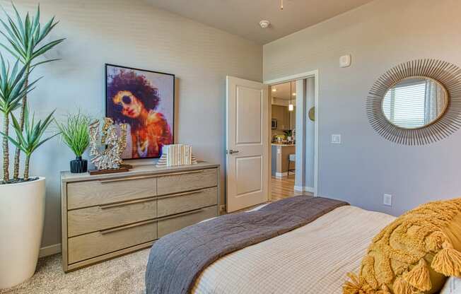 South Scottsdale Apartments - Lucent Scottsdale - Spacious Bedroom With Carpeted Flooring, Bed, Dresser, Arts, and Plants