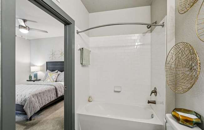 A bathroom with a white tub and a bedroom with a bed and a ceiling fan.