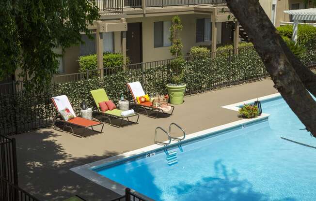 a swimming pool with lounge chairs and a tree in front of a building
