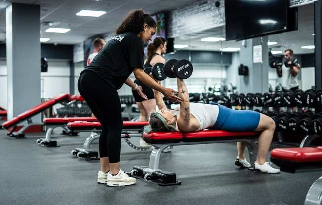 a man laying on a bench in a gym with a woman holding a dumbbell