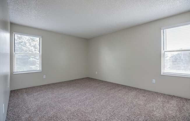 an empty room with carpet and two windows