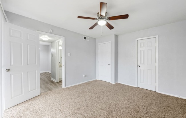 an empty bedroom with a ceiling fan and white doors