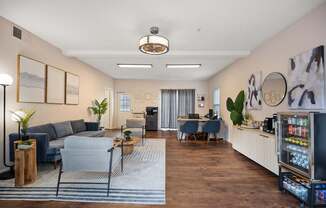 A modern living room with a grey sofa, a coffee table, and a kitchenette in the background.