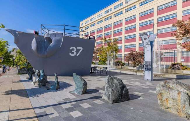 A large grey sculpture of a ship with the number 37 on it is in the foreground of a city square at Spyglass Hill Apartments, Bremerton, 98337