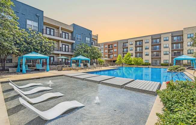 a swimming pool with lounge chairs and an apartment building in the background