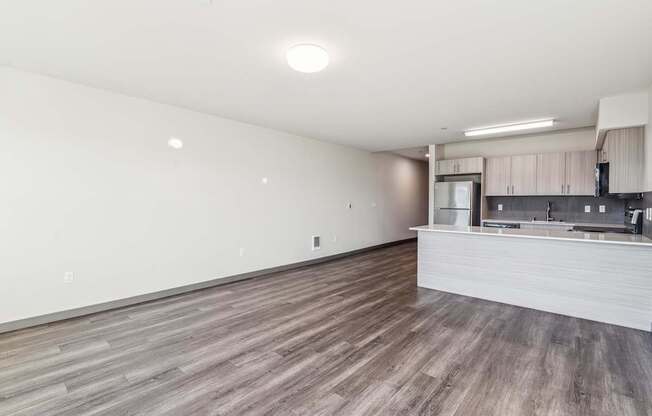 A spacious room with wooden flooring and a kitchen area in the background.