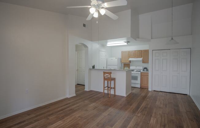 an empty living room with a kitchen and a ceiling fan