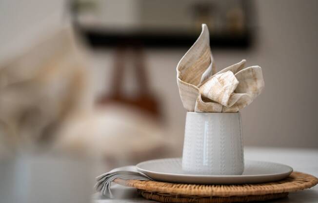 a white cup with a napkin on top of a plate on a table