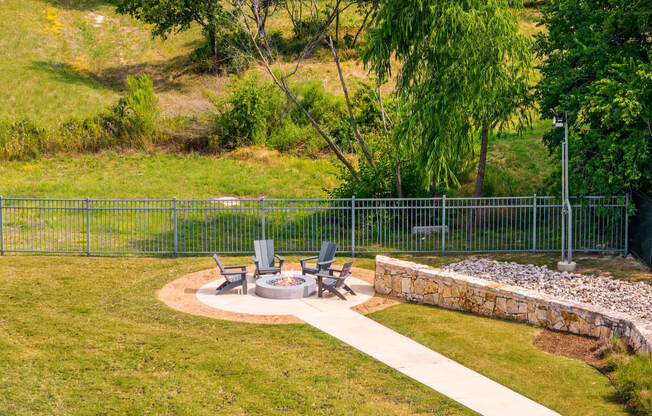a fire pit in the middle of a grassy area with chairs and a stone wall