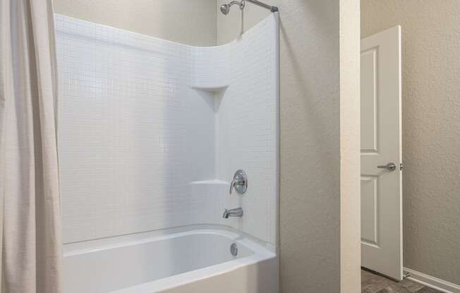 A white bathtub with a shower head and a curtain.