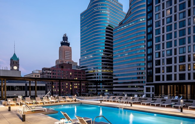 A rooftop pool with lounge chairs and a city skyline in the background.