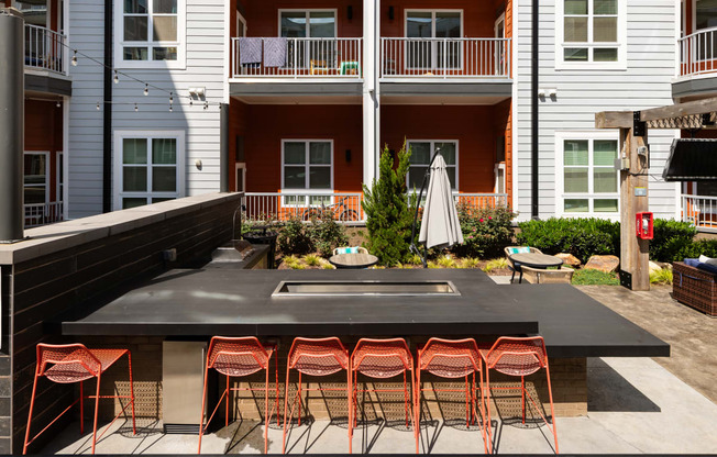 an outdoor kitchen with a bar and stools in front of an apartment building  at Abberly Noda Vista Apartment Homes, North Carolina, 28206