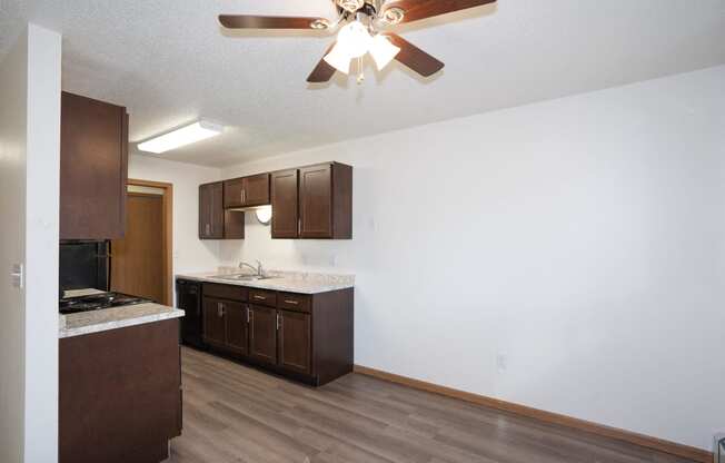 an empty kitchen with wooden cabinets and a ceiling fan. Fargo, ND Country Club Apartments