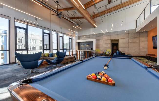 Community Clubhouse Pool Table with Blue Chairs, Brown Sofa and Hanging Ceiling Lights