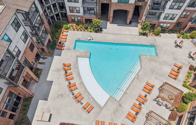 A swimming pool surrounded by orange lounge chairs in a courtyard.