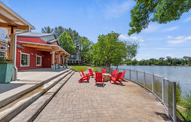 A red building with a white roof is situated next to a body of water with a red bench in front of it.