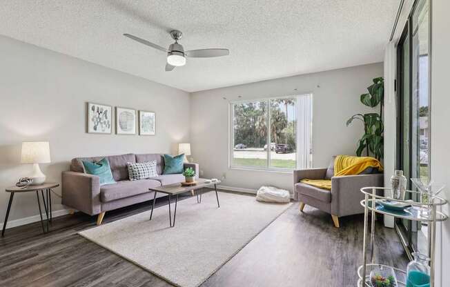 A living room with a grey couch, a yellow chair, and a white ceiling fan.