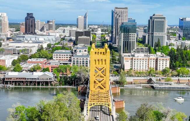 A yellow bridge spans a river in a city with a mix of modern and older buildings.