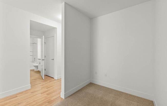 A white room with a carpet and a doorway leading to another room.