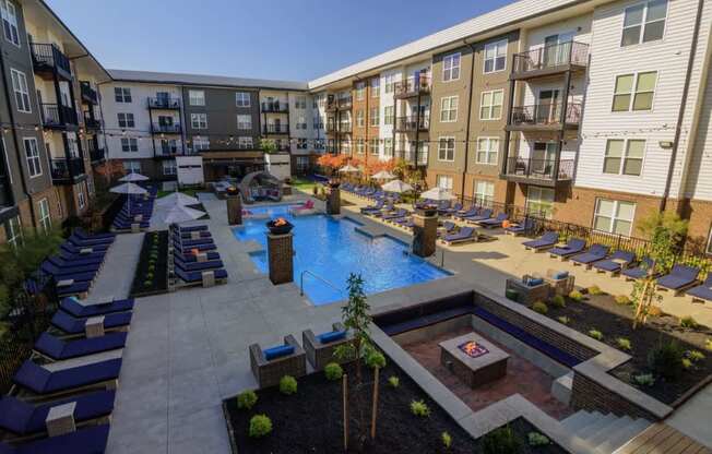 A large outdoor pool area with lounge chairs and a hot tub surrounded by apartment buildings.