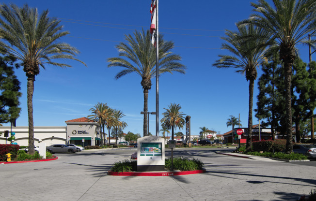 A sign in front of palm trees with a flag in the background.