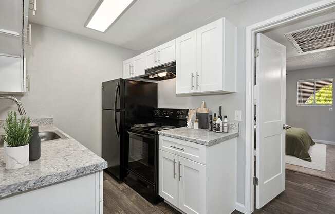 Model Kitchen with White Cabinets and Wood-Style Flooring with Bedroom Entrance at Stillwater Apartments in Glendale, AZ.