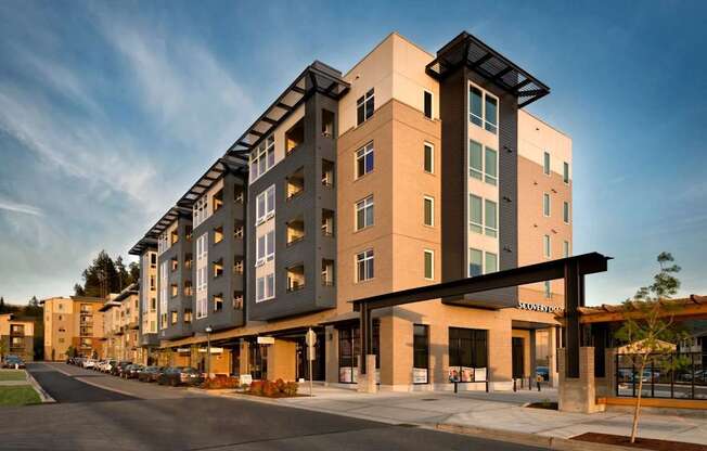 A modern multi-story building with a parking lot in front.