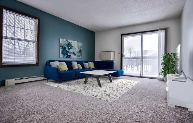 Grand Forks Primrose Apartment.  A living room with a blue couch and coffee table in front of a sliding glass door