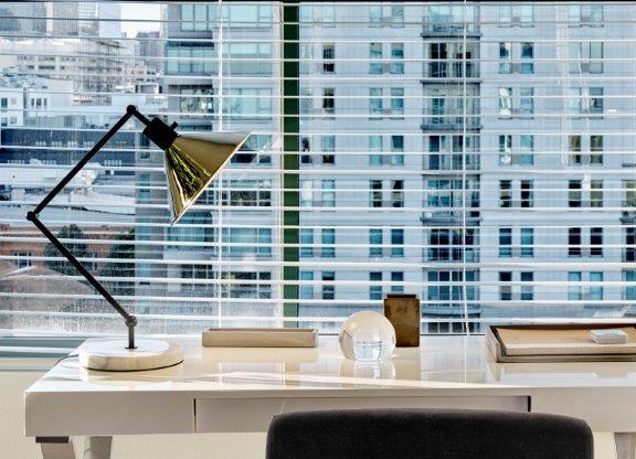 A black chair sits in front of a desk with a lamp on it.